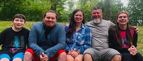 Nichole Plaggue sits next to her husband and 3 children and all smile at the camera.